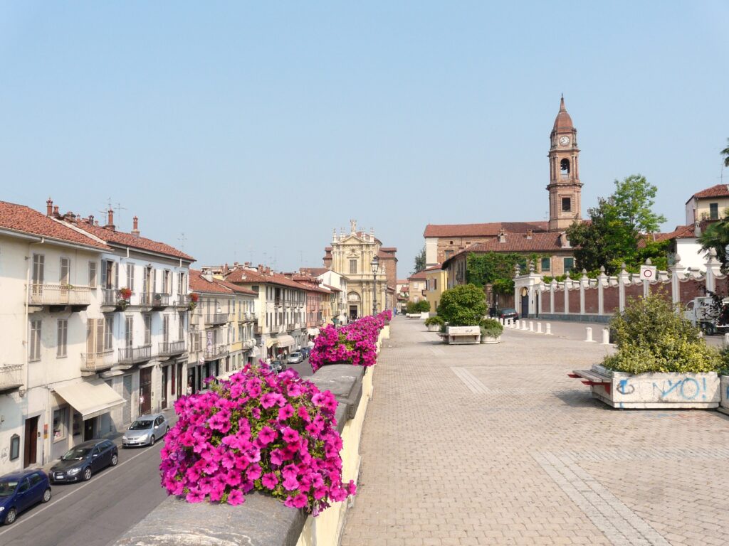 A View of the city of Bra in Piedmont, Italy with bright pink flowers, buildings to the left and a church in the near distance