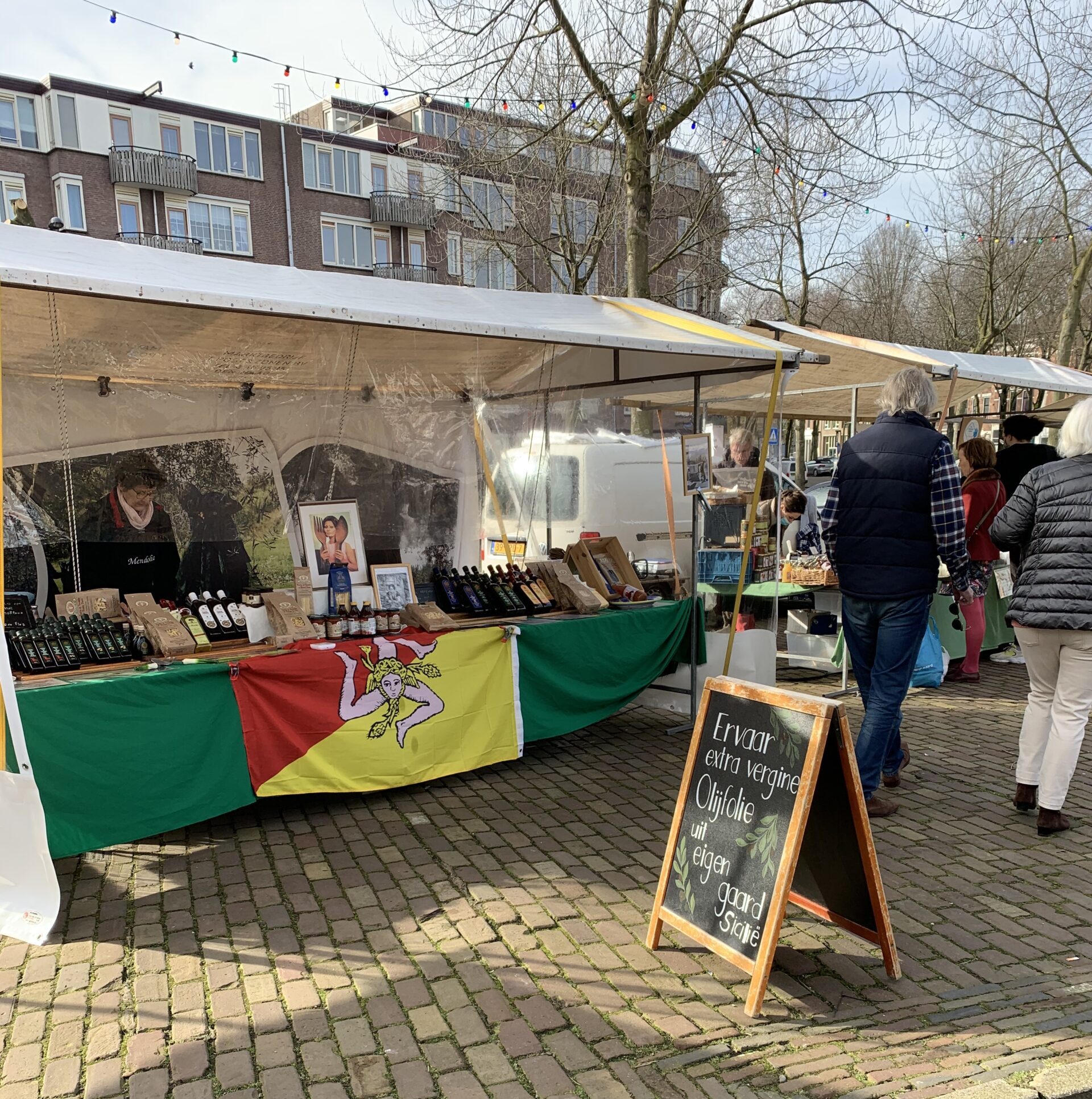 Market stall with a sign in front announcing that it sells extra virgin olive oil