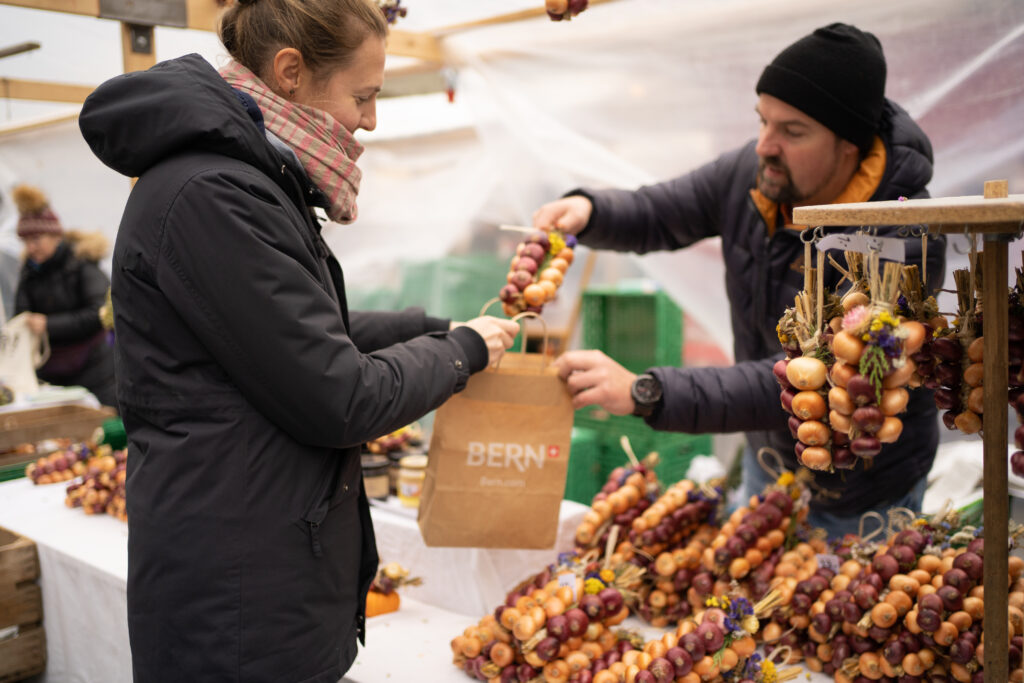 Onion Market Bern Man wearing hat handing a paper bag to a woman in daylight