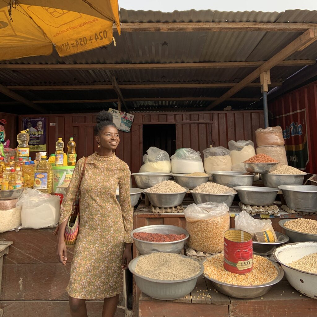 woman standing under parasol at african market next to bowls of spices in daylight