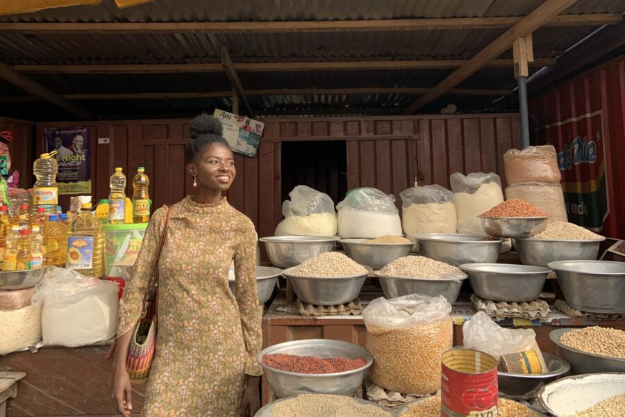 woman standing under parasol at african market next to bowls of spices in daylight