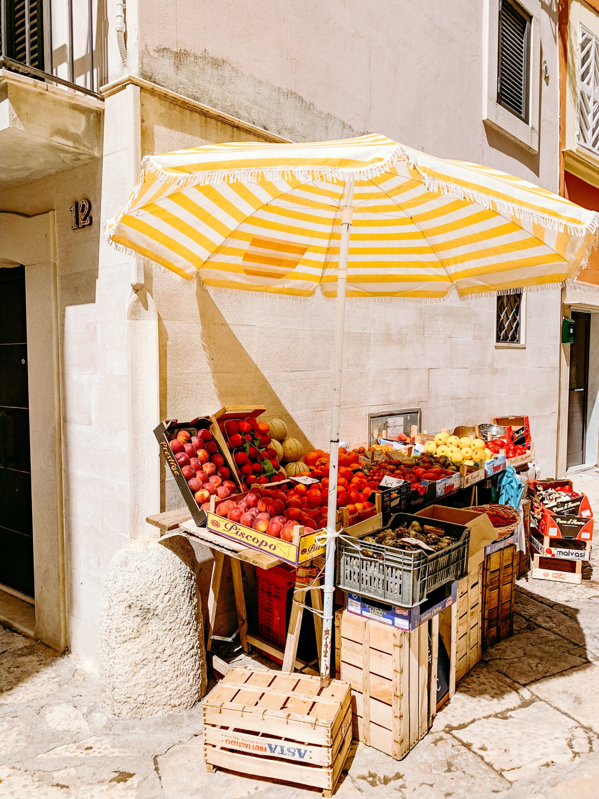 advertise markets yellow striped parasol with crates of fruit underneath on street corner